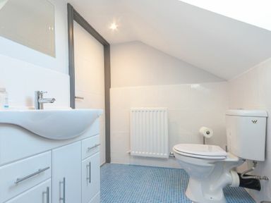 A bathroom with a sink on a cabinet a toilet a radiator and a door at Riverview Alnmouth