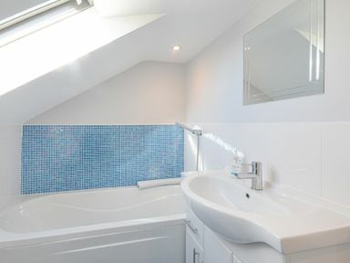 A bathroom with a bathtub sink mirror and blue tiled wall at Riverview Alnmouth