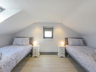 A bedroom with two single beds and two nightstands with lamps under a window at Riverview Alnmouth