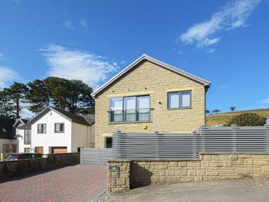 A stone house with a grey fence and a paved driveway at Riverview Alnmouth