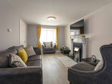 A living room with gray sofas yellow curtains and a wall-mounted TV at Coastal View in Seahouses