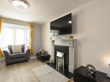 A living room with an armchair yellow curtains a fireplace and a wall mounted TV at Coastal View in Seahouses