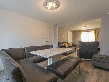 A dining area with a corner bench and a table next to a living room with sofas and yellow curtains at Coastal View in Seahouses