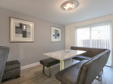 A dining area with a rectangular table surrounded by bench seats and a chair with two framed abstract artworks on the wall at Coastal View in Seahouses