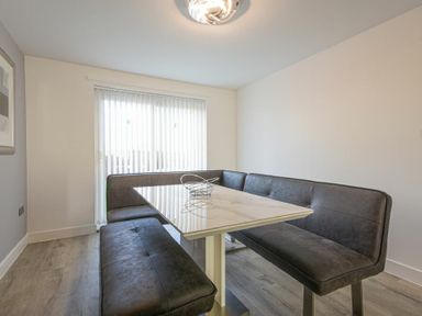 A dining area with a rectangular table and corner bench seating with vertical blinds covering the window at Coastal View in Seahouses
