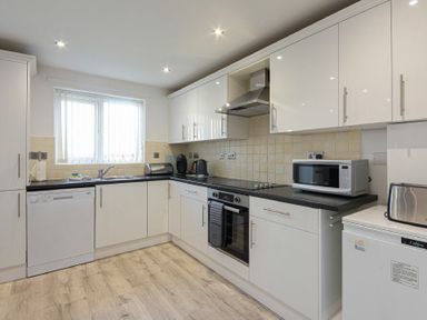 A kitchen with white cabinets black countertops and appliances at Coastal View in Seahouses