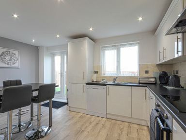 A kitchen and dining area with a black table and chairs a dishwasher and white cabinets at Coastal View in Seahouses