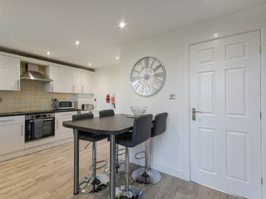 A kitchen with a black countertop island and bar stools and white cabinetry at Coastal View in Seahouses