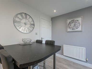 A dining area with a black table and chairs a wall clock and a framed picture at Coastal View in Seahouses