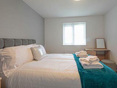 A bedroom with a bed covered in white linens and folded towels on a blue blanket at Coastal View in Seahouses