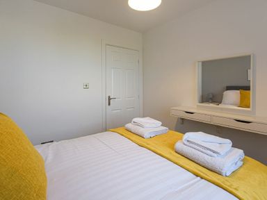 A bedroom with a bed with white and yellow bedding a door and a wall-mounted dresser with a mirror at Coastal View in Seahouses