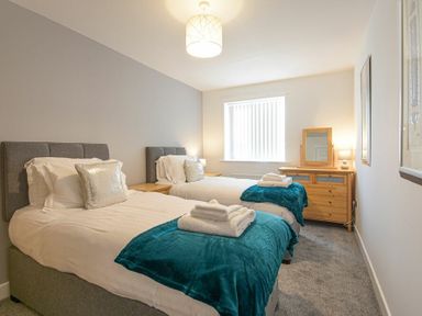 A bedroom with two single beds with blue throws and folded towels and a wooden dresser with a mirror at Coastal View in Seahouses