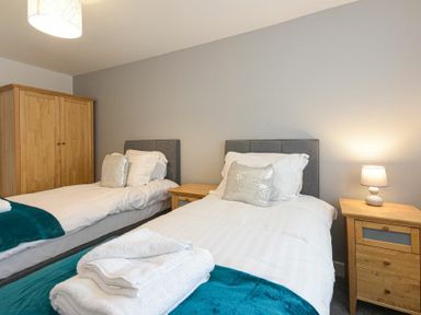 A bedroom with two single beds wooden bedside tables a wooden wardrobe and a lamp at Coastal View in Seahouses