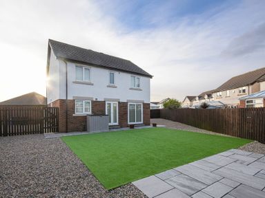 A backyard with a green lawn gravel areas and a paved patio behind a two-story house with a white and brick exterior Coastal View in Seahouses