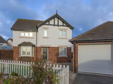 A two story house with brick and white facade and a detached garage behind a white picket fence at Coastal View in Seahouses