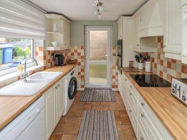 A galley kitchen with wooden countertops dishwasher washing machine sink and stove at Five Bells Cottage in Alnmouth