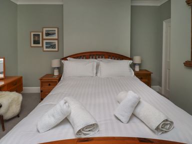 A bedroom with a wooden bed and two bedside tables with lamps and rolled towels on the bed at Five Bells Cottage in Alnmouth