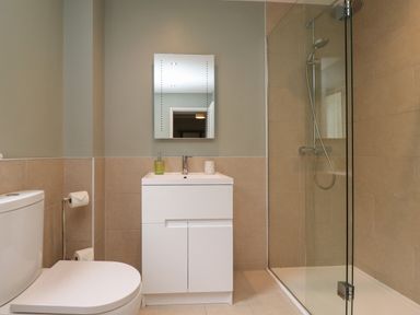 A bathroom with a toilet, a white vanity with a mirror above, and a glass-enclosed shower at Five Bells Cottage in Alnmouth