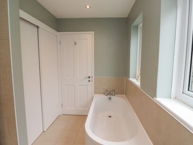 A bathroom with a bathtub next to a window and a door at Five Bells Cottage in Alnmouth