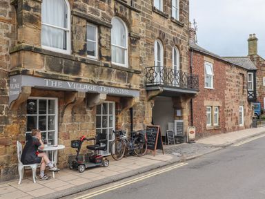 The exterior of The Village Tearooms with a person sitting at a small table outside a stone building in Alnmouth