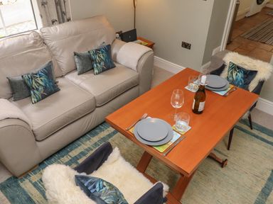 A seating area with a beige sofa and two chairs around a wooden dining table set with plates glasses and a bottle at Five Bells Cottage in Alnmouth