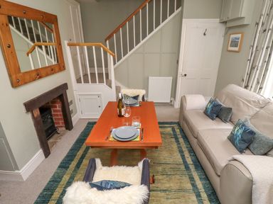 A living room with a beige sofa a wooden table set for two and a staircase at Five Bells Cottage in Alnmouth