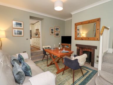A living room with a sofa small dining table two chairs a rug a fireplace and a television at Five Bells Cottage in Alnmouth