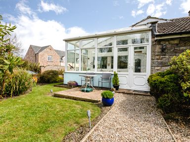 A patio with table and chairs next to a glass conservatory and garden path at Palmers Rest in Beadnell