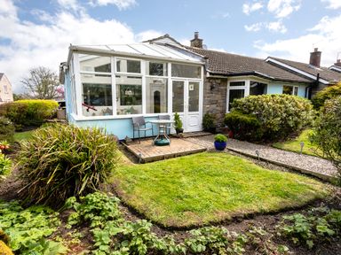 A garden with shrubs and a conservatory attached to a house at Palmers Rest in Beadnell