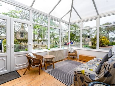 A sunroom with two wicker chairs a small table a couch with patterned cover a rug and a telescope at Palmers Rest in Beadnell