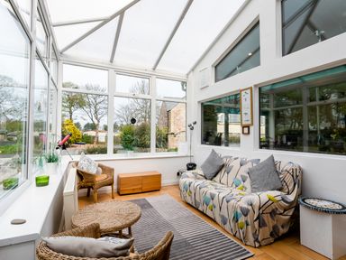 A sunroom with wicker chairs a sofa with patterned cover and large windows at Palmers Rest in Beadnell