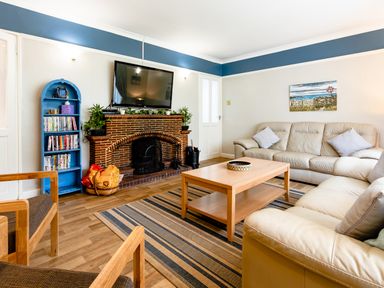 A living room with leather sofas a wooden coffee table a brick fireplace and a TV mounted above at Palmers Rest in Beadnell