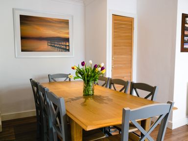 A dining room with a wooden table and gray chairs and a vase of tulips on the table at Palmers Rest in Beadnell