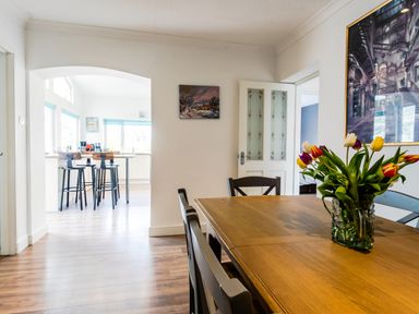 A dining room with a wooden table and chairs and a vase of tulips with a kitchen and bar stools visible through an archway at Palmers Rest in Beadnell