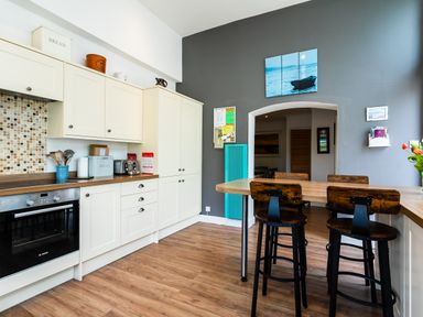 A kitchen with white cabinets wooden countertop a mosaic tile backsplash an oven three wooden bar stools and a dining table at Palmers Rest in Beadnell