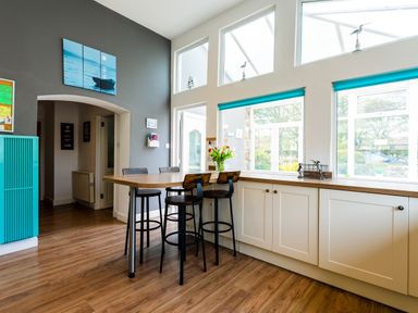 A kitchen area with a wooden breakfast bar and stools next to large windows at Palmers Rest in Beadnell
