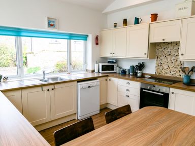 A kitchen with white cabinets blue window blind wooden table and chairs at Palmers Rest in Beadnell