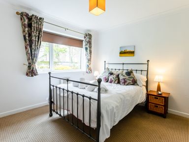 A bedroom with a metal bed frame floral curtains and bedside table with lamp at Palmers Rest in Beadnell