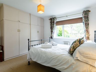 A bedroom with a bed with white linen and floral pillows a window with floral curtains and built-in wardrobes at Palmers Rest in Beadnell