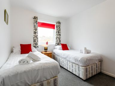 A bedroom with two single beds a window with curtains and a red blind and a small wooden bedside table at Palmers Rest in Beadnell