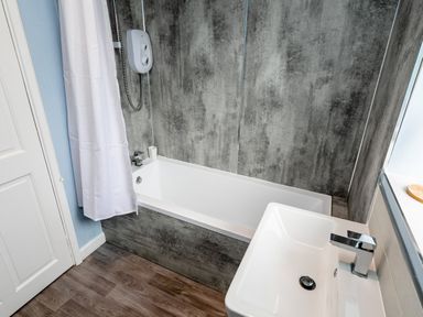 A bathroom with a bathtub shower combination white curtain and a sink with a modern faucet at Palmers Rest in Beadnell