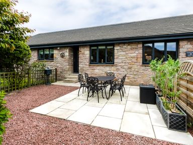 A stone exterior house with black metal outdoor table and chairs on a stone patio at Polished Pebble in Beadnell