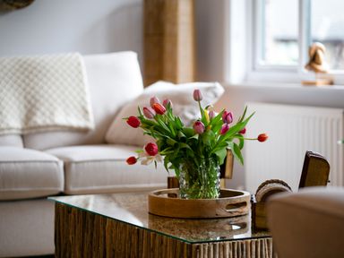 A living room with a vase of pink and red tulips on a glass coffee table at Polished Pebble in Beadnell