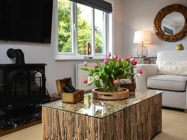 A living room with a glass-topped wooden coffee table holding a vase of tulips and wooden chests near a gray sofa at Polished Pebble in Beadnell