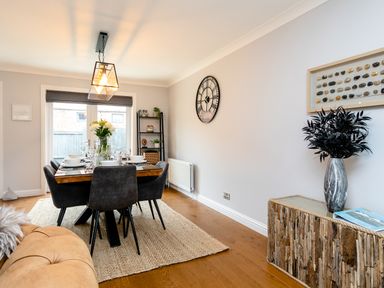 A dining room with a wooden table and black chairs a large wall clock and a shelf unit at Polished Pebble in Beadnell