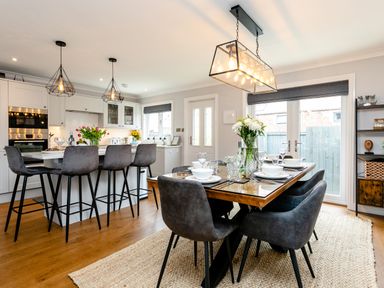 A kitchen and dining area with bar stools and a dining table set with dishes at Polished Pebble in Beadnell