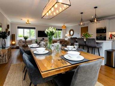 A dining area with a set table and flowers next to a living room and kitchen at Polished Pebble in Beadnell