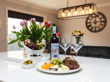 A kitchen counter with a bottle of wine cheese grapes bread olives and tulips at Polished Pebble in Beadnell