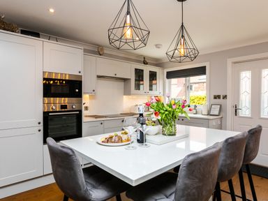 A kitchen with white cabinetry a central island with chairs and pendant lights at Polished Pebble in Beadnell