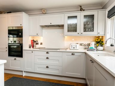 A kitchen with white cabinets a built in oven glass fronted cupboards and kitchen appliances at Polished Pebble in Beadnell